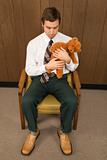 Man sitting in chair holding a stuffed animal looking sad.