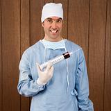 Male surgeon smiling holding giant syringe.