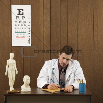 Male doctor at desk writing.