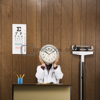Doctor at desk holding clock over face.