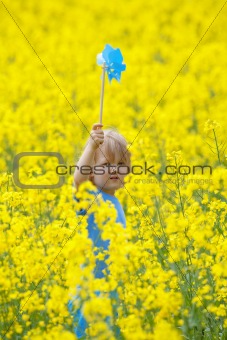 boy with long blond hair holding pinwheel in canola field