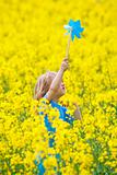 boy with long blond hair holding pinwheel in canola field