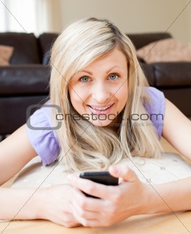 Delighted woman sending a text lying on a bed at home