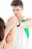 Concentrated physical therapist checking a woman's shoulder