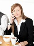 Worried businesswoman talking on phone while having breakfast 