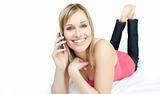 Cheerful woman talking on phone lying on a bed 