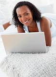 Cheerful woman using a laptop on her bed