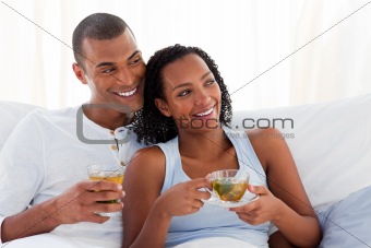 Jolly couple drinking a cup of tea on their bed