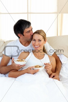 Affectionate couple eating cereals lying in the bed