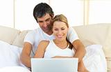 Enamoured couple using a laptop lying in the bed