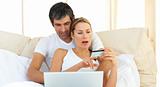 Loving couple using a laptop lying in the bed