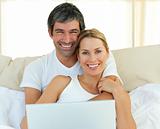 Smiling couple using a laptop lying in the bed