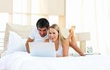 Joyful lovers using laptop lying on bed