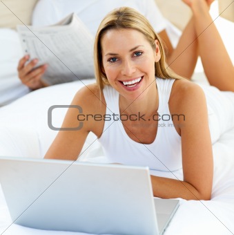 Smiling woman using a laptop lying on bed