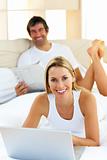 Smiling couple lying on bed using computer