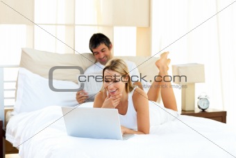 Positive woman using a laptop lying on bed