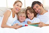 Smiling family reading a book on bed