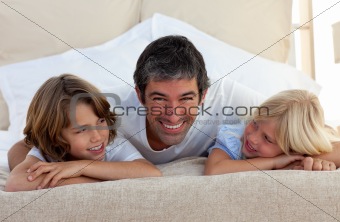 Smiling father talking with his children lying on bed