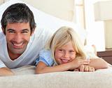 Smiling little girl having fun with her father lying on bed