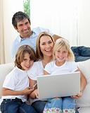 Happy family using a laptop sitting on sofa at home