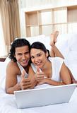 Happy couple surfing the internet lying on their bed