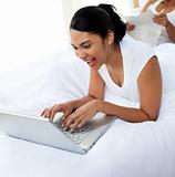 Happy woman using a laptop lying on the bed