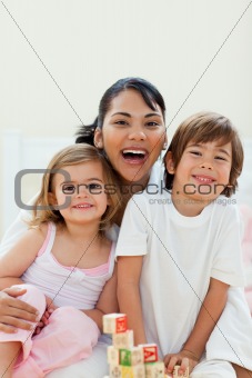 Cute children kissing their mother sitting on a bed at home