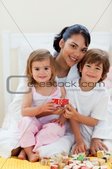 Smiling siblings and their mother playing with letter blocks 