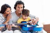Cute little boy playing guitar with his parents 