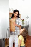 Cheerful little girl unpacking grocery bag with her mother