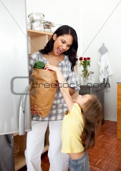 Blond little girl unpacking grocery bag with her mother