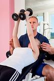 young woman lifting weights in modern gym with trainer