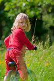 boy with long blond hair riding a bike in the garden