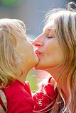 mother kissing her son with long blond hair outdoors