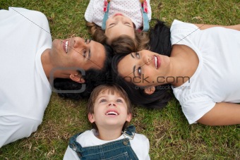 Joyful family lying in a circle on the grass 