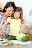 Adorable little girl cutting vegetables with her mother