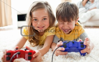 Jolly children playing video games lying on the floor with their parents in the background