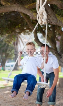 Happy father pushing his son on a swing in a park