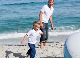 Happy father and his son playing with a ball at the beach