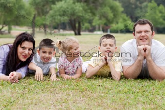 Cheerful family of five lying on lawn in the green park 