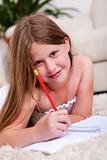 Smiling young girl lying and writing in notebook