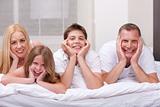 Beautiful family lying on bed smiling and looking at you