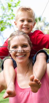 Close-up of a mother giving her son a piggyback ride in a park 
