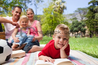 Little boy reading lying on a picnic tablecloth 