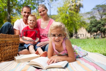Cute little girl reading lying on the grass while having a picni