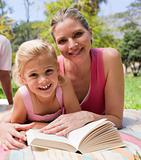 Happy mother and her daughter reading in a park
