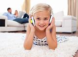 Happy little girl listening music lying on the floor