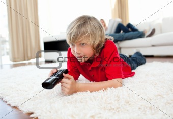 Cute boy holding a remote lying on the floor 