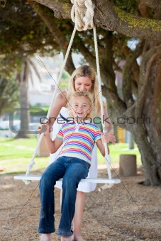 Happy mother pushing her daughter on a swing 
