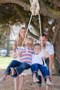 Joyful parents pushing their children on a swing 